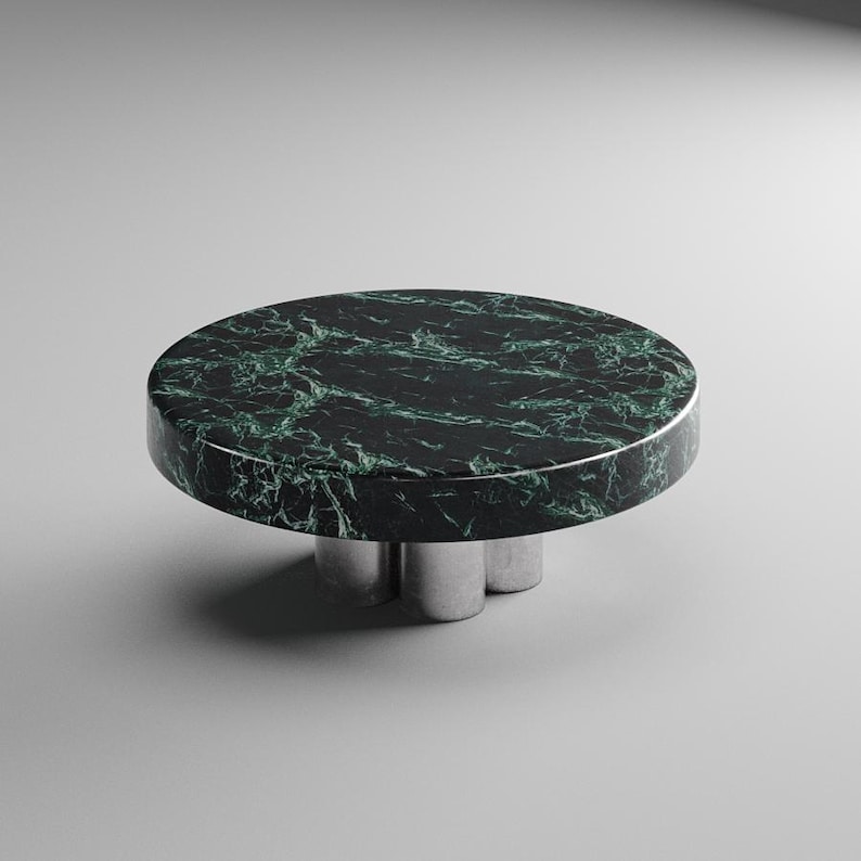 May include: A round, low table with a dark green marble top and a silver-colored, three-legged base. The marble has a striking veined pattern. The table is a modern design, suitable for a living room or lounge area.