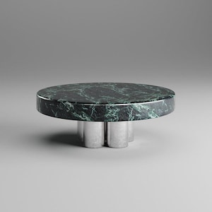 May include: A round coffee table with a dark green marble top and a silver metal base. The marble has white veining. The base has a unique, three-legged design. The table is a modern, minimalist design.