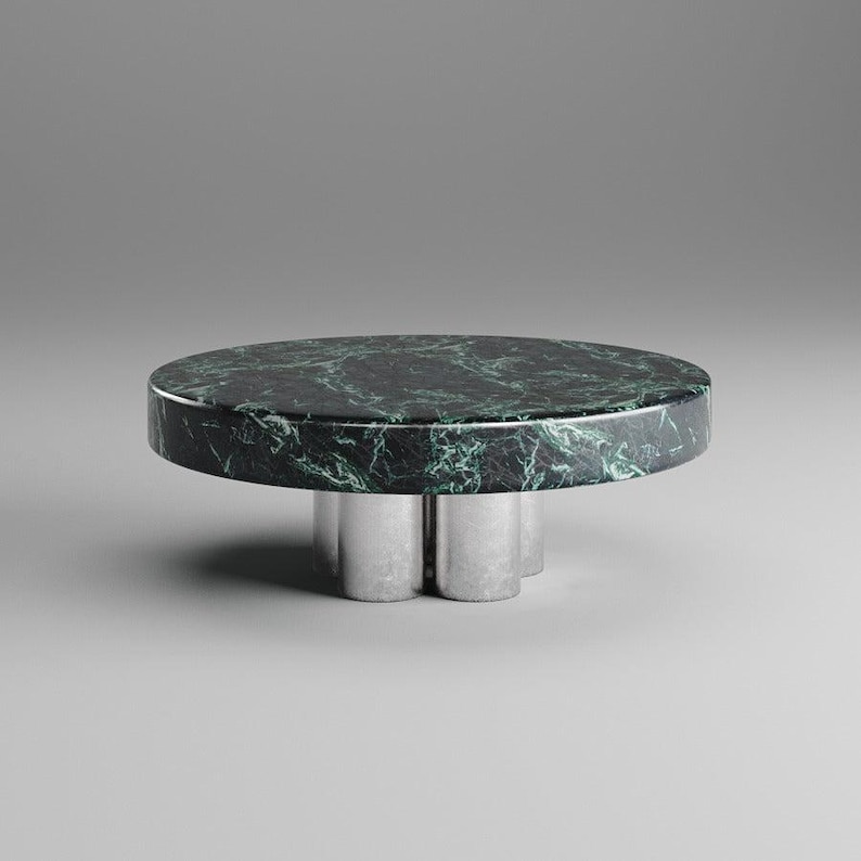 May include: A round coffee table with a dark green marble top and a silver metal base. The marble has white veining. The base has a unique, three-legged design. The table is a modern, minimalist design.