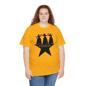 Peut inclure: Un t-shirt jaune avec une silhouette noire de trois femmes dansant sur une étoile noire avec le mot "FIDDLER" en texte noir.