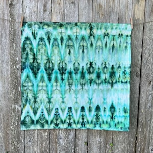 May include: A green and white tie-dye fabric with a chevron pattern. The fabric is hanging on a wooden fence.