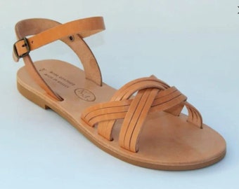 Può includere: Sandali in pelle color cuoio con un designo a cinturino intrecciato e un cinturino alla caviglia con chiusura a fibbia. I sandali hanno una suola piatta e sono realizzati in Grecia.