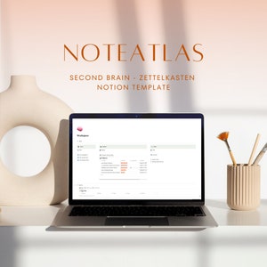 Könnte beinhalten: Ein Laptop-Computer, auf dem ein Notion-Arbeitsbereich mit dem Titel "Noteatlas - Second Brain - Zettelkasten Notion Template" angezeigt wird. Der Laptop steht auf einem weißen Tisch mit einer beigefarbenen Vase und Pinseln.