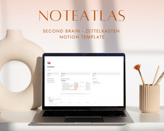 May include: A laptop computer displaying a Notion workspace with the title "Noteatlas - Second Brain - Zettelkasten Notion Template". The laptop is on a white table with a beige vase and paintbrushes.