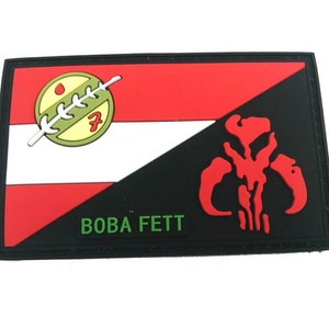 May include: Rectangular patch with a diagonal split design. One side has a red, white, and green emblem, the other a red skull on black. The text "BOBA FETT" is printed in green, a Star Wars themed item.