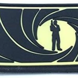 May include: Black and yellow embroidered patch with a silhouette of a person holding a gun inside a swirling target design.