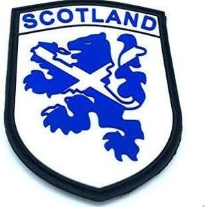 Op de afbeelding: Een witte en blauwe geborduurde patch met het woord "SCOTLAND" in zwarte letters. De patch toont een blauwe leeuw die een wit Andreaskruis vasthoudt.