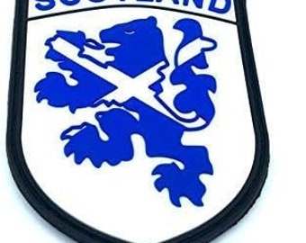 May include: A white and blue embroidered patch with the word "SCOTLAND" in black lettering. The patch features a blue lion rampant holding a white saltire cross.