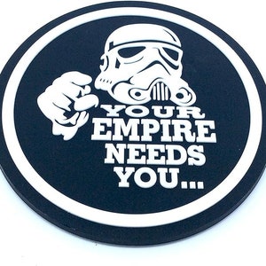 Peut inclure: Un dessous de verre rond noir et blanc avec un casque de Stormtrooper et une main pointant. Le texte "YOUR EMPIRE NEEDS YOU..." est en blanc, dans un bord blanc.