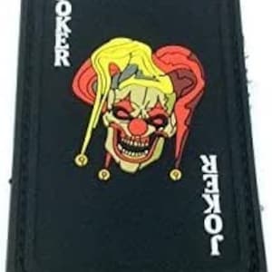 May include: Black patch with a white border and the word "JOKER" printed vertically on the left and right sides. A red and yellow joker face with a toothy grin is in the centre.