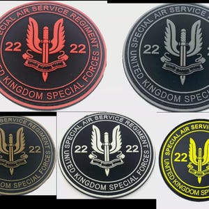 May include: Five circular patches displaying the text "UNITED KINGDOM SPECIAL FORCES" and "SPECIAL AIR SERVICE REGIMENT". Each patch features a central design with a sword and wings, and the number "22". The patches are in different color combinations, including red, grey, gold, and yellow.
