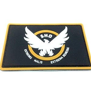May include: A rectangular black morale patch with a yellow border. The centre features a white eagle graphic inside a yellow circle, with the text SHD above the eagle and the Latin phrase EXTREMIS MALIS EXTREMA REMEDIA printed below it.