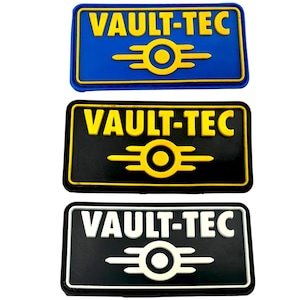 May include: Three Vault-Tec patches, one blue, one black with yellow text, and one black with white text. Each patch features the Vault-Tec logo with the text "Vault-Tec" above it.
