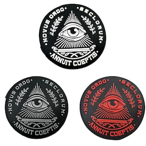 May include: Three black and white circular patches with a white eye inside a triangle, surrounded by a wreath and the text "NOVUS ORDO SECLORUM. ANNUIT COEPTIS."