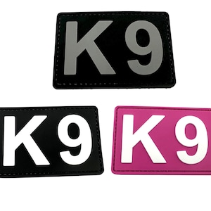 Pode incluir: Três patches K9 de cores diferentes. O primeiro patch é preto com letras cinzas. O segundo patch é preto com letras brancas. O terceiro patch é rosa com letras brancas.