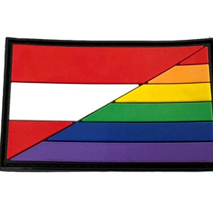 May include: A black-bordered patch with a red, white, and rainbow design. The rainbow is arranged in a diagonal pattern, with the red and white stripes of the Austrian flag above it.