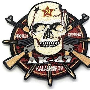 Può includere: Una toppa ricamata in rosso, bianco e nero con un teschio con una stella rossa sulla fronte. Il teschio è circondato da due fucili AK-47 incrociati con le parole "Proteggi" e "Difendi" su entrambi i lati. Il testo "AK-47 Kalashnikov" è scritto sotto il teschio.