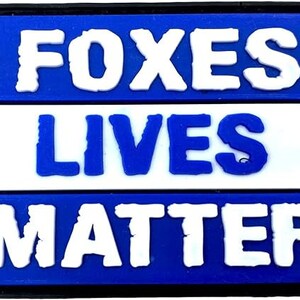May include: Blue and white patch with the text "Foxes Lives Matter" in bold white letters.