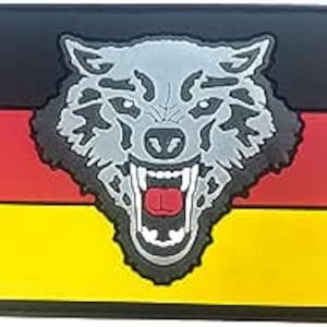 May include: A black, red and yellow patch with a grey wolf's head in the centre. The wolf has a snarling expression and its mouth is open, revealing its teeth. The patch is made of a rubber-like material.