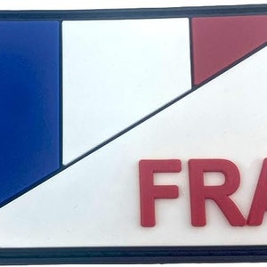 Può includere: Una toppa bianca con un design a strisce diagonali blu, bianco e rosso. La parola "FRA" è stampata in lettere rosse sulla toppa.