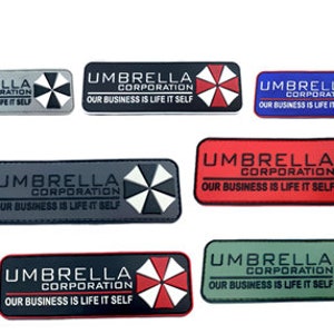 May include: Set of ten embroidered patches featuring the Umbrella Corporation logo and the text "Umbrella Corporation, Our Business Is Life Itself". The patches are in various colours, including black, grey, red, blue, and green.