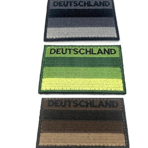 May include: Three embroidered patches with the word "DEUTSCHLAND" across the top. Each patch features horizontal stripes in different color schemes: black to gray, green to yellow, and brown to tan. The patches are rectangular.