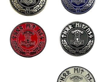 May include: Five circular metal pins with a Viking theme. Each pin displays a hammer symbol at the centre, encircled by text and patterns. The pins are available in black, blue, red, grey, and white.