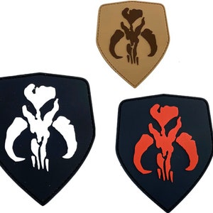 Op de afbeelding: Drie geborduurde patches in de vorm van een schild met een Mandaalorian symbool. De patches zijn zwart met een wit symbool, zwart met een rood symbool en bruin met een bruin symbool.