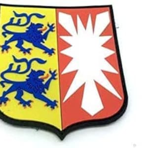 Może przedstawiać: Naszywka haftowana na żółto i czerwono z herbem przedstawiającym dwa niebieskie lwy i białą gwiazdę.