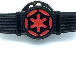 Könnte beinhalten: Schwarze Emaille-Anstecknadel mit einem roten imperialen Symbol und Flügeln. Die Nadel hat eine silberne Rückseite mit einem Sicherheitsverschluss.