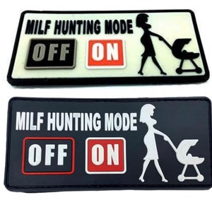 Op de afbeelding: Twee zwart-witte patches met de tekst "MILF HUNTING MODE" en een schakelaar met de woorden "OFF" en "ON". De schakelaar staat op "ON". De patches tonen een wit silhouet van een vrouw die een kinderwagen duwt.