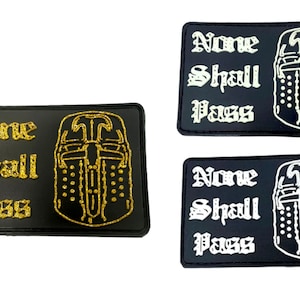 Puede incluir: Dos parches negros con el texto "None Shall Pass" en letras doradas y blancas. Cada parche presenta un casco de caballero con una espada.