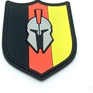 Può includere: Una toppa a forma di scudo nero, rosso e giallo con un elmo spartano argentato al centro.