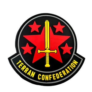 Op de afbeelding: Een zwarte en grijze ronde patch met een rode ster in het midden. De ster heeft vijf punten en een geel zwaard in het midden. De tekst "TERRAN CONFEDERATION" staat in een gele boog rond de ster.