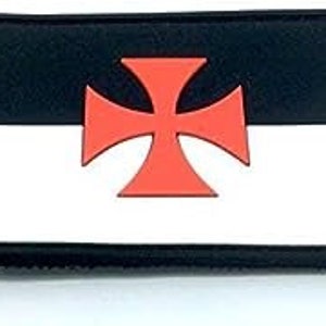 Peut inclure: Un patch noir et blanc avec une croix rouge au centre. Le patch est en tissu et a un dos en velcro.