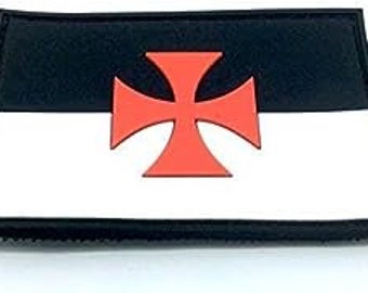 May include: A black and white patch with a red cross in the center. The patch is made of fabric and has a velcro backing.