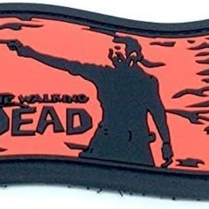 May include: A black and red patch featuring a silhouette of a person pointing a gun. The text "The Walking Dead" is printed in white on the patch.