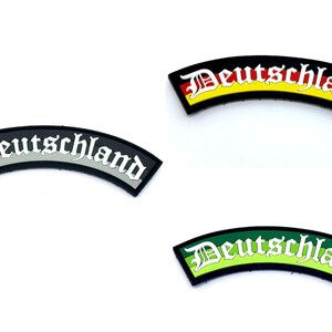 May include: Three black and white embroidered patches with the word "Deutschland" in a gothic font. The patches have different coloured backgrounds: red, yellow and green.