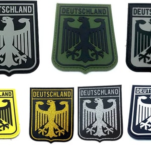 May include: Set of 8 iron-on patches featuring the German coat of arms with the words "DEUTSCHLAND" in black lettering. The patches are in various colours including black, white, grey, green, yellow, and gold.