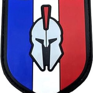 May include: A blue, white and red shield-shaped patch with a white Spartan helmet in the centre. The helmet has a red plume.