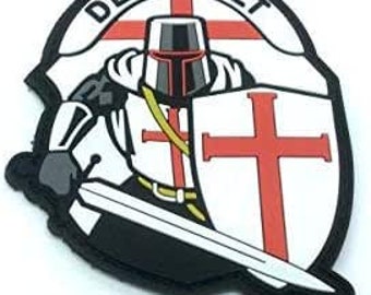 May include: A white and red embroidered patch featuring a knight in armour holding a sword and shield. The shield displays a red cross on a white background. The knight is wearing a white helmet with a red cross. The patch is inscribed with the words "Deus Vult" around the edge.