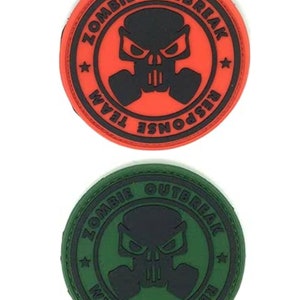 Peut inclure: Deux patchs ronds brodés en noir et blanc avec le texte "Zombie Outbreak Response Team" et un crâne portant un masque à gaz. Le patch du haut est rouge et le patch du bas est vert.
