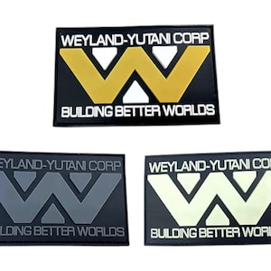 Può includere: Tre toppe nere con testo bianco e un logo 'W' stilizzato. Il testo recita 'Weyland-Yutani Corp' e 'Building Better Worlds'. Il logo 'W' è in oro, grigio e bianco.