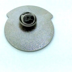 May include: The back of a silver metal pin with a safety clasp.