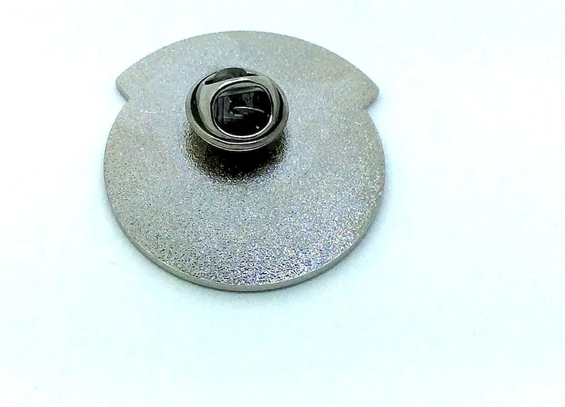 May include: The back of a silver metal pin with a safety clasp.