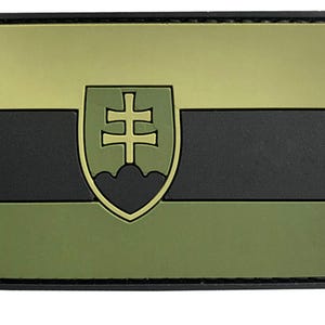 May include: A rectangular morale patch featuring a horizontal tricolor design in shades of olive green and black. Centered on the patch is a shield emblem displaying a double-barred cross above a three-peaked mountain silhouette in olive green.
