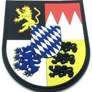 Peut inclure: Un écusson brodé représentant les armoiries de la Bavière, en Allemagne. L'écusson est en forme de bouclier et présente un lion, un motif en losange et trois montagnes.