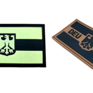 May include: Two versions of a black and tan fabric patch with the German flag and the text "DEU". One patch is a standard colour and the other is glow-in-the-dark.