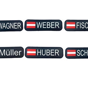 May include: Six black rectangular name tags with the Austrian flag and white text. The names are Wagner, Weber, Fischer, Müller, Huber, and Schmidt.