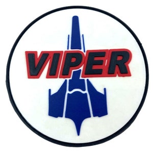 Peut inclure: Un écusson circulaire blanc avec une bordure noire. Au centre de l'écusson se trouve un vaisseau spatial stylisé bleu et blanc avec le mot "VIPER" en lettres rouges et noires.